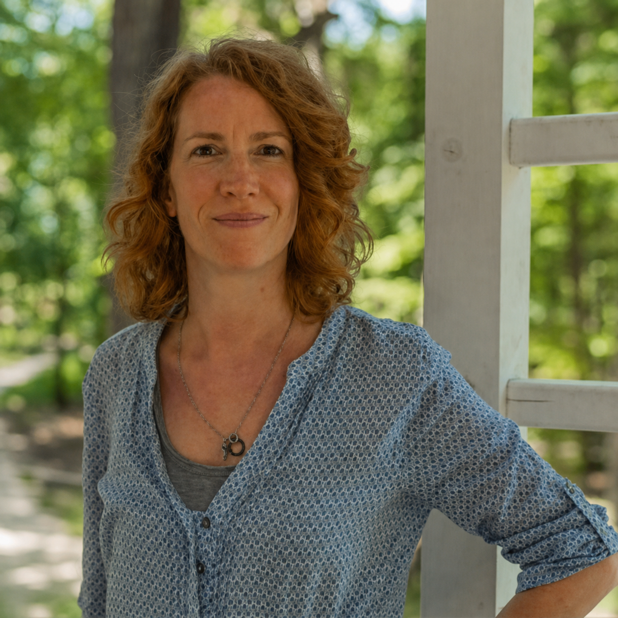Aurélie Schwartz, consultante en bilan de compétences, souriante devant une véranda entourée de verdure.